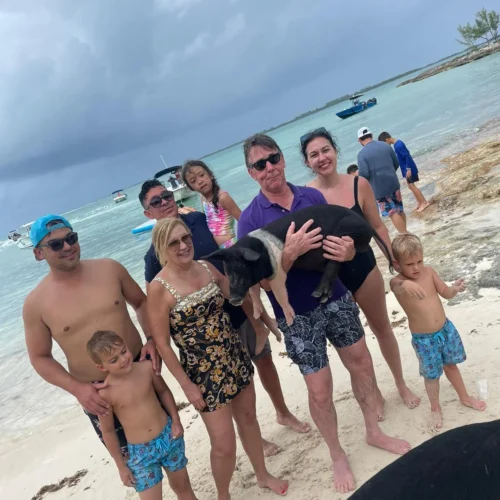 Family standing on a white sand beach with the charter boat anchored offshore near Nassau, Bahamas