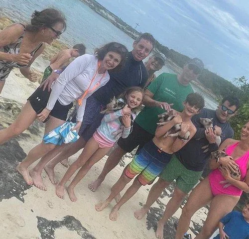 Smiling family on the beach cradling baby swimming pigs near Nassau, Bahamas