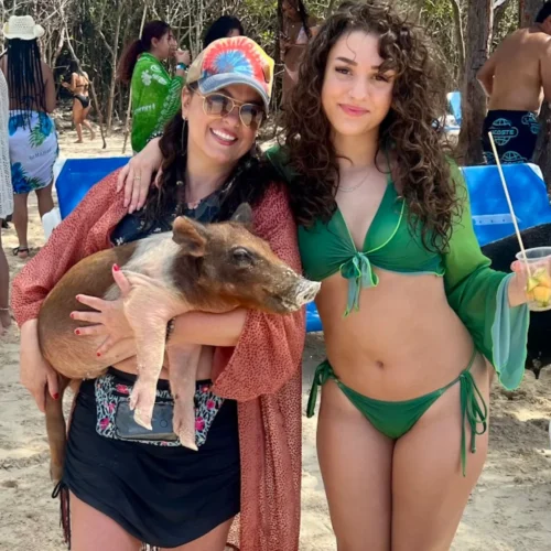 Two smiling women beside a swimming pig on the beach near Nassau, Bahamas