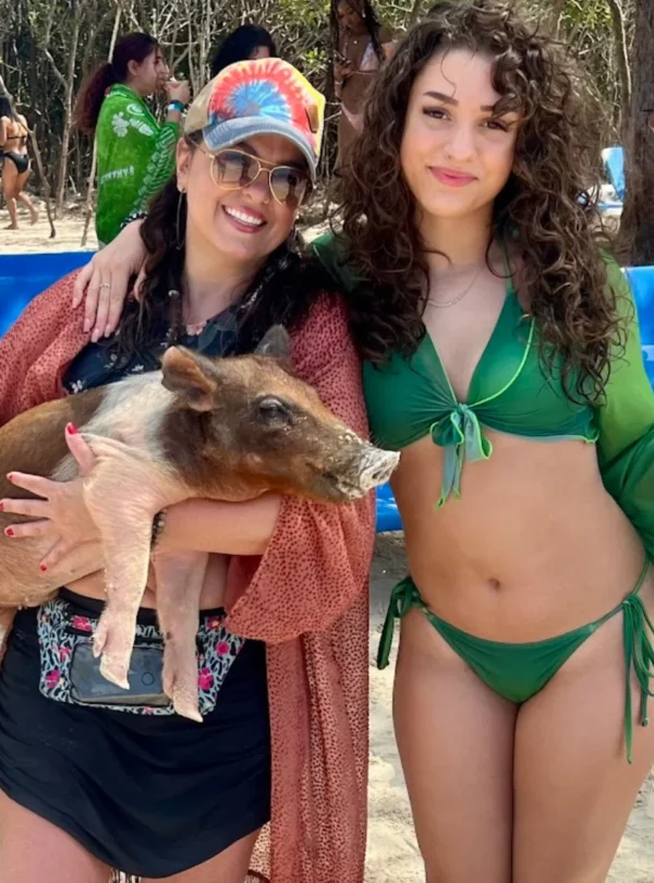 Two smiling women beside a swimming pig on the beach near Nassau, Bahamas