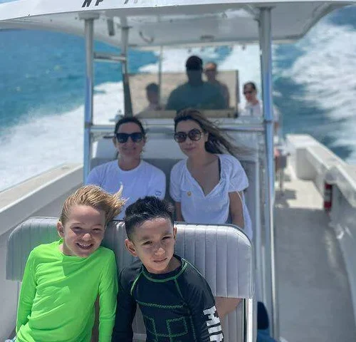Two smiling kids at the front of a private charter boat cruising over blue water near Nassau, Bahamas