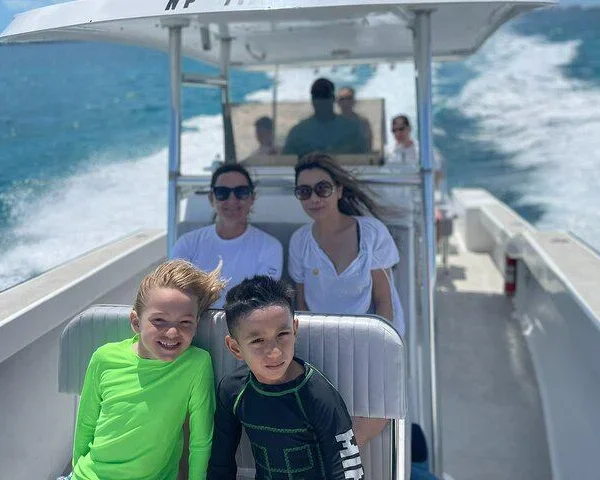 Two smiling kids at the front of a private charter boat cruising over blue water near Nassau, Bahamas