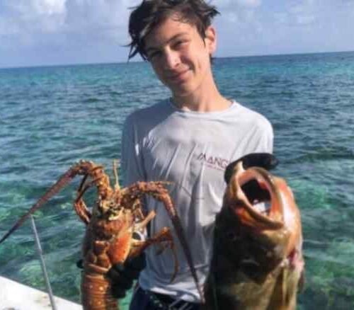 Young guest holding a lobster and a fish on the boat near Nassau, Bahamas